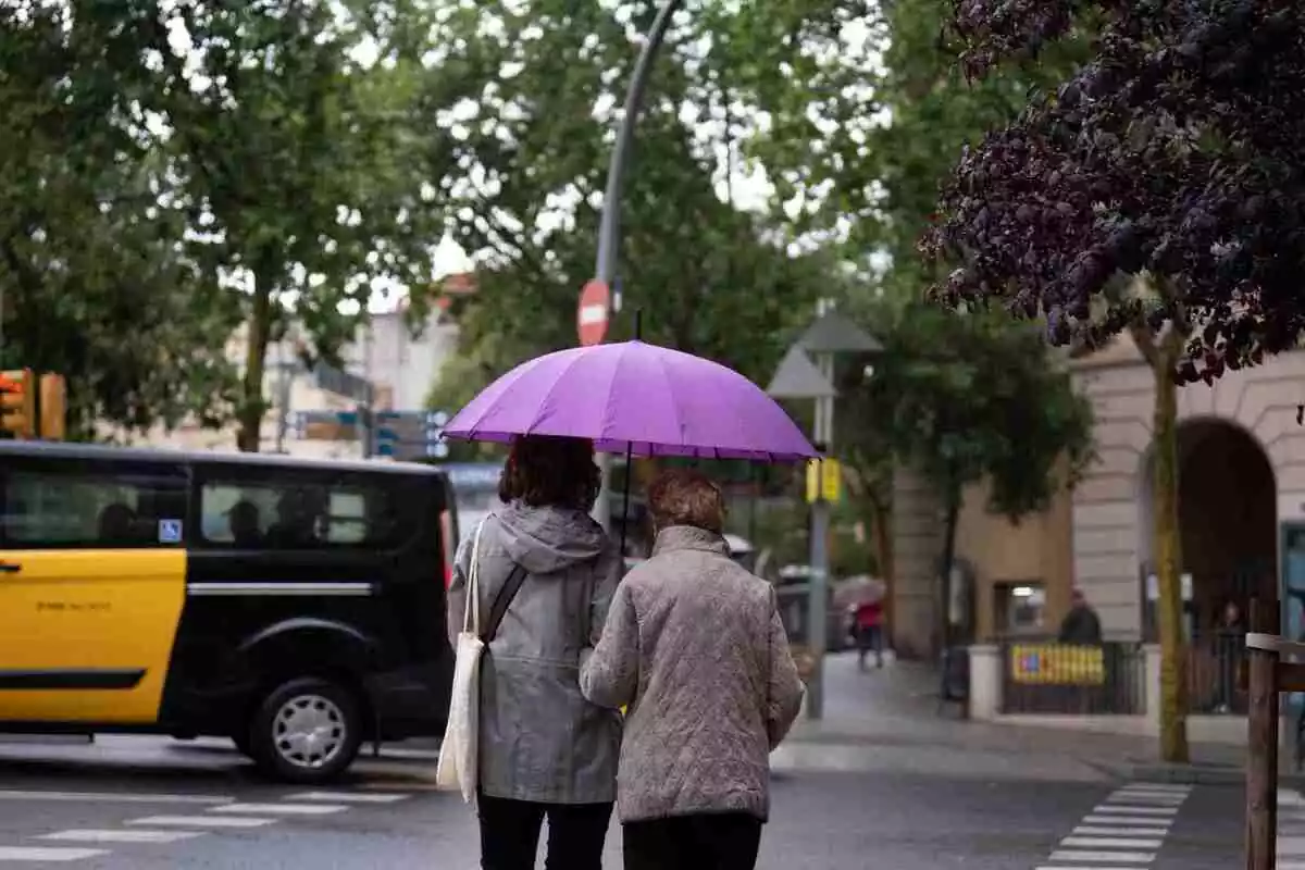 Imatge de dues persones amb un paraigua passejant per Barcelona