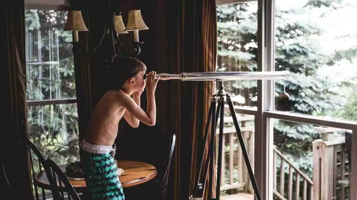 Un nen mirant pel telescopi des de la finestra de casa