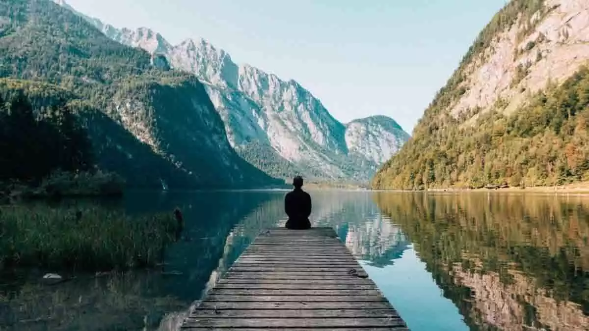 Home reflexionant entre montanyes i un llac