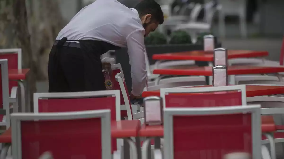 Un cambrer netejant una cadira envoltat de taules i cadires vermelles el 12 de març de 2020