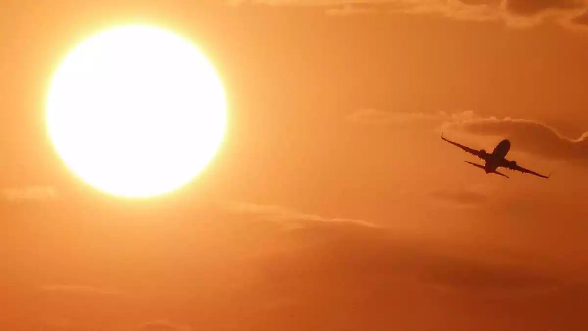 Imatge d'un avió creuant el cel amb el sol de fons