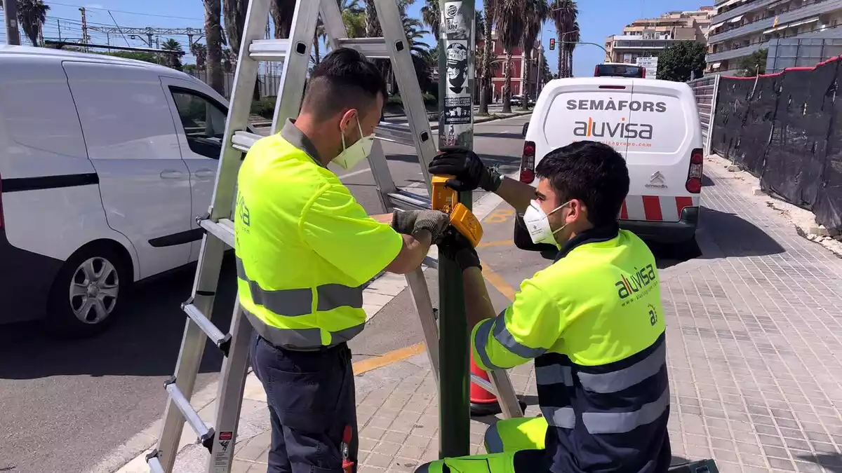 Imatge d'uns operaris canviant la botonera d'un semàfor a la carretera N-II a Mataró perquè es pugui activar amb el colze