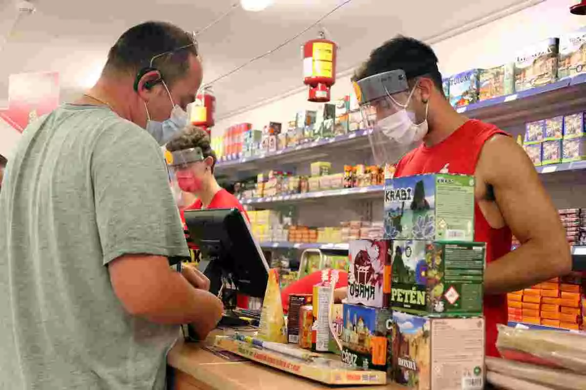 Pla mitjà d'un empleat de Petards CM atenent un client amb mascareta el dia 15 de juny de 2020 a la botiga de Palau-solità