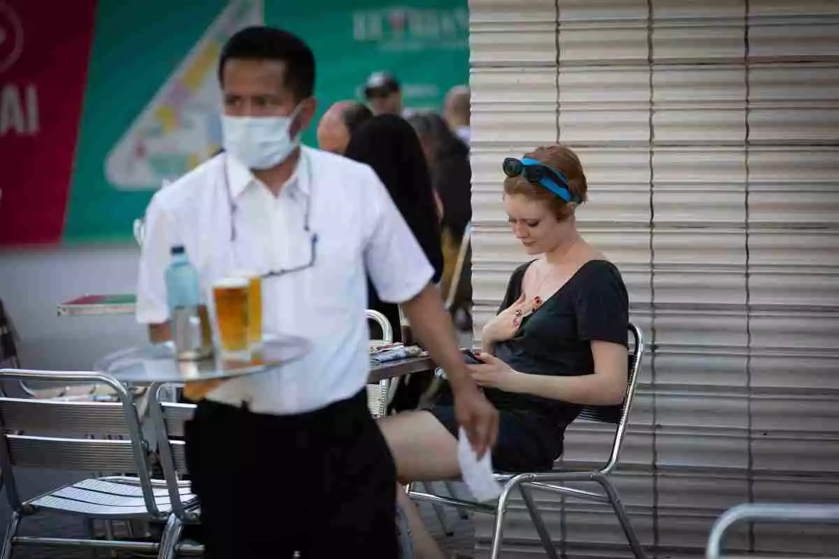Un cambrer amb mascareta serveix una cervesa en una terrassa de Barcelona