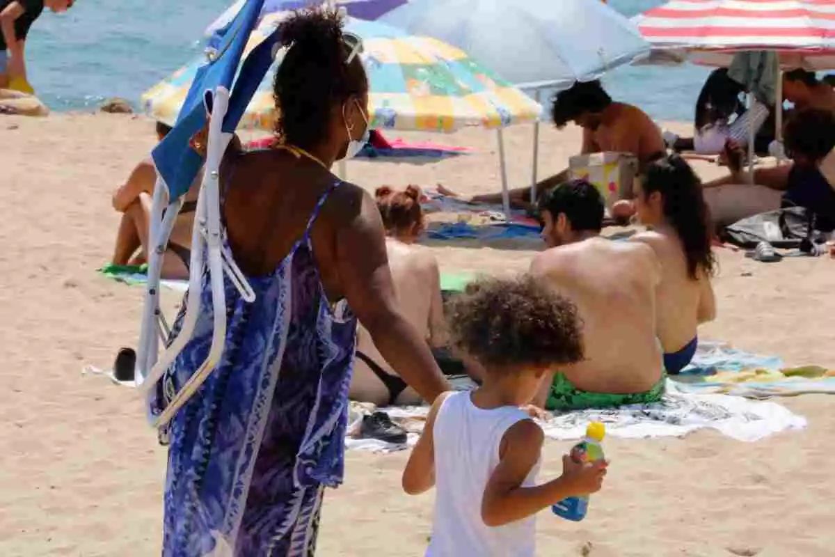 Una dona camina per la platja de la Nova Icària de Barcelona, agafant un nen de la mà