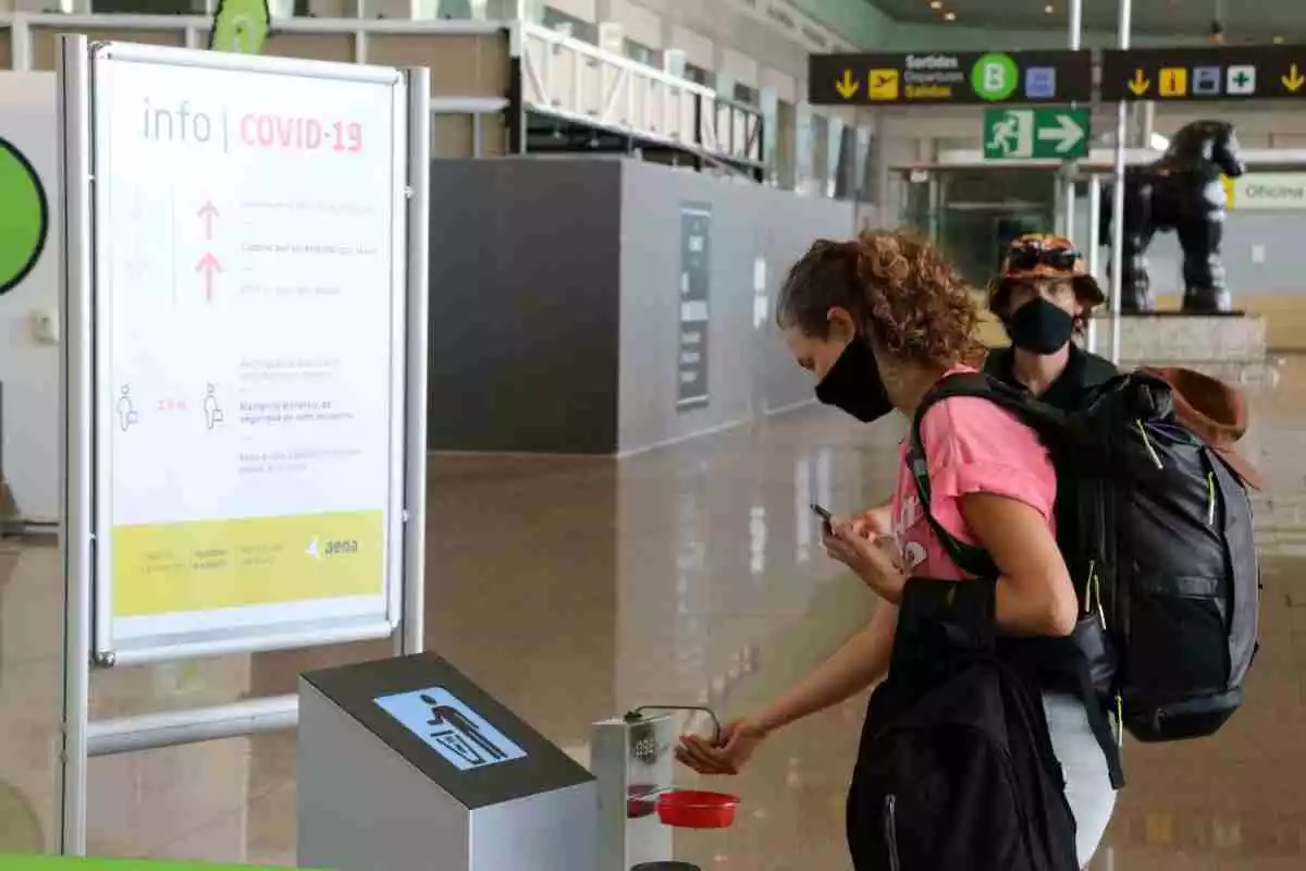 Pla mitja d'una passatgera de la terminal 2 de l'Aeroport del Prat netejant-se les mans a l'entrada de les instal·lacions