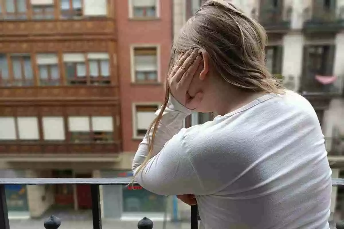 Imatge d'una dona, vestida amb jersei blanc, en un balcó durant el confinament