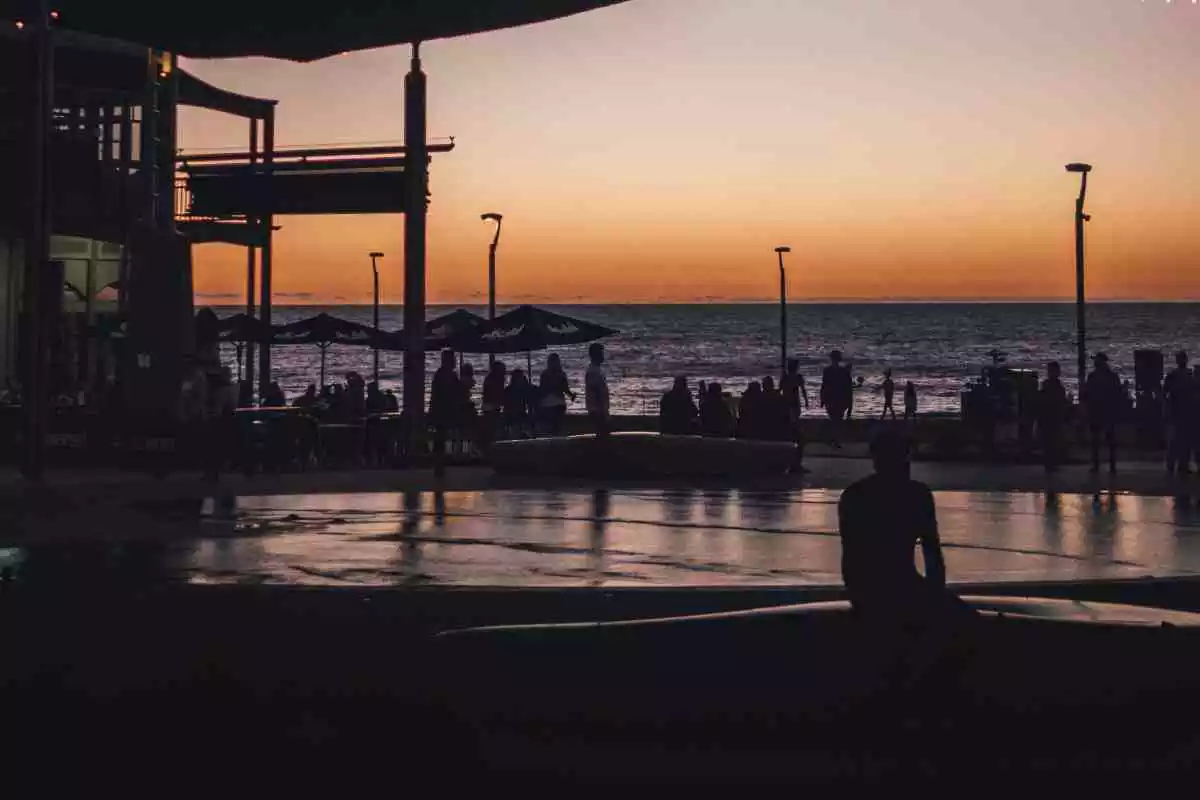 Gent gaudint de la posta de sol en un passeig marítim