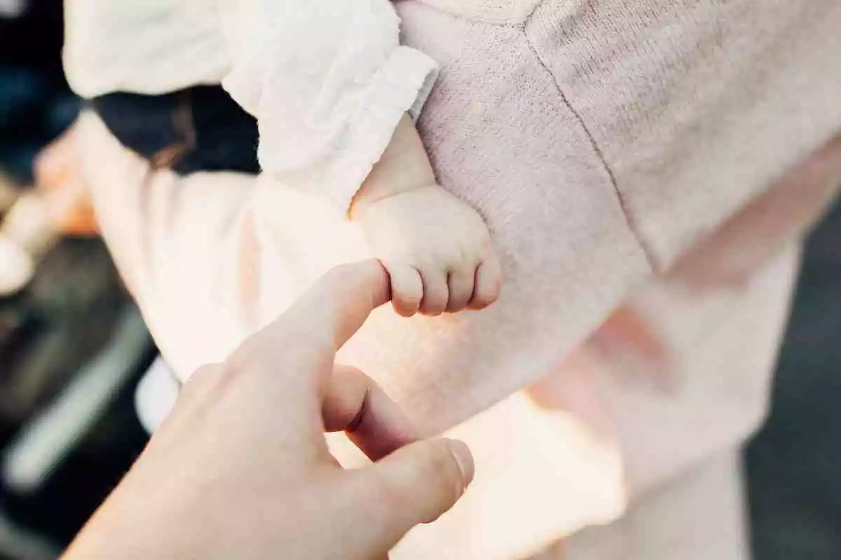 La mà d'un nadó agafant-ne una altre