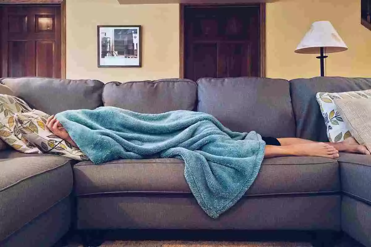 Persona tumbada al sofà de casa seva amb una manta