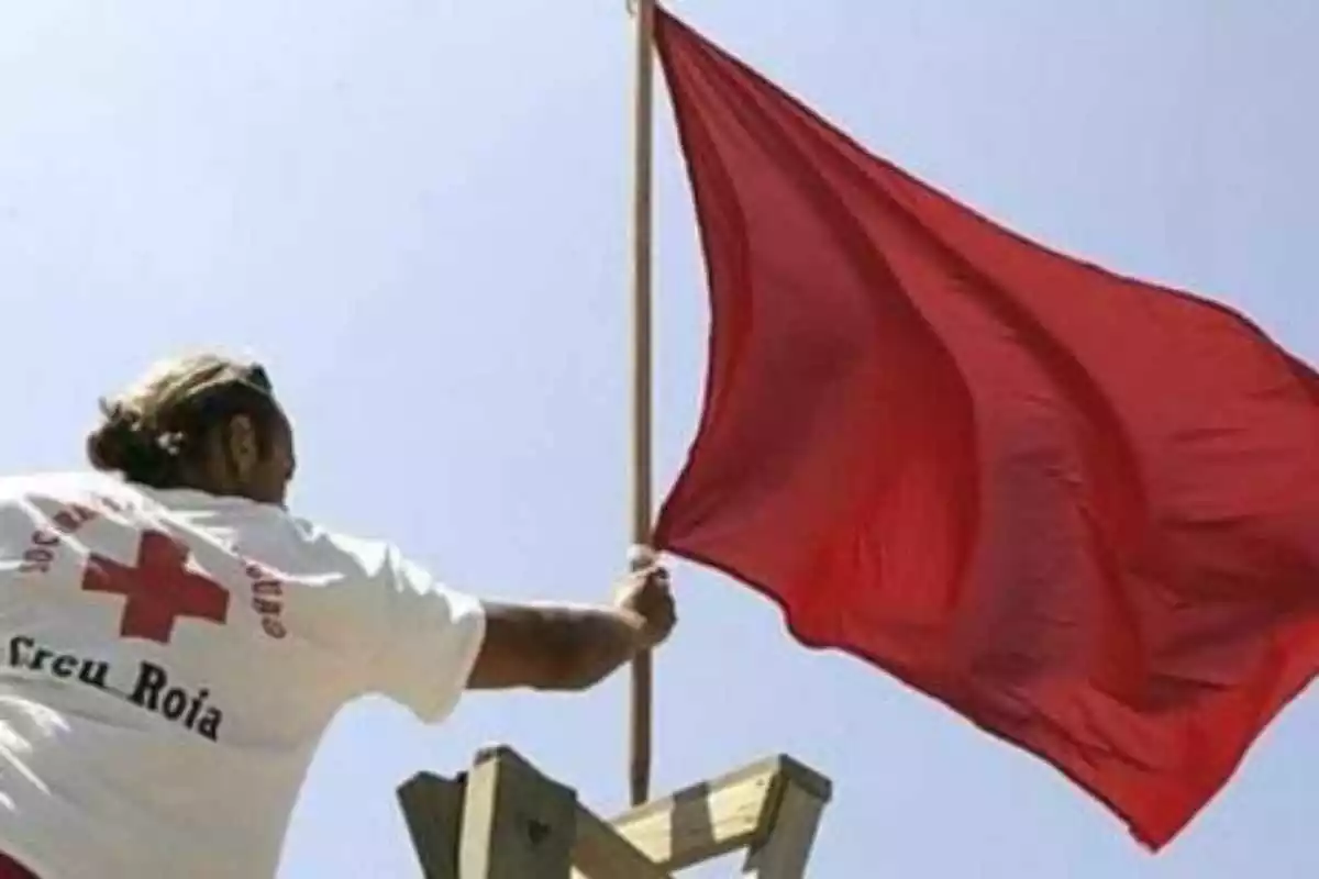 Imatge d'un socorrista hissant la bandera vermella en una platja