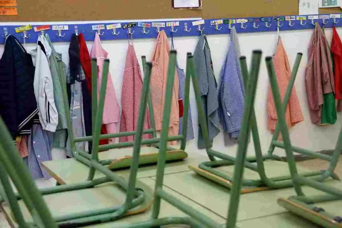 Renglera de bates al penjador d'una escola i cadires sobre les taules