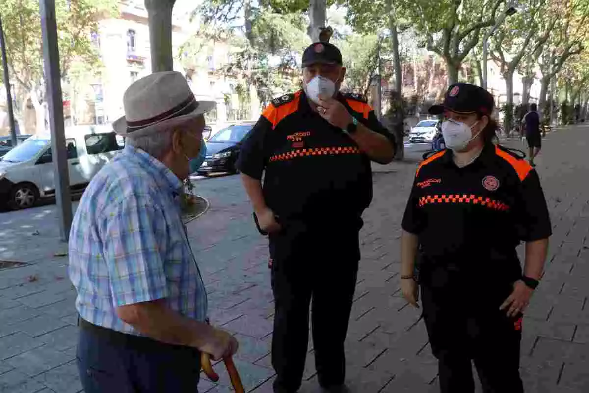 Dos agents de Protecció Civil amb mascareta aconsellant un home gran a Reus