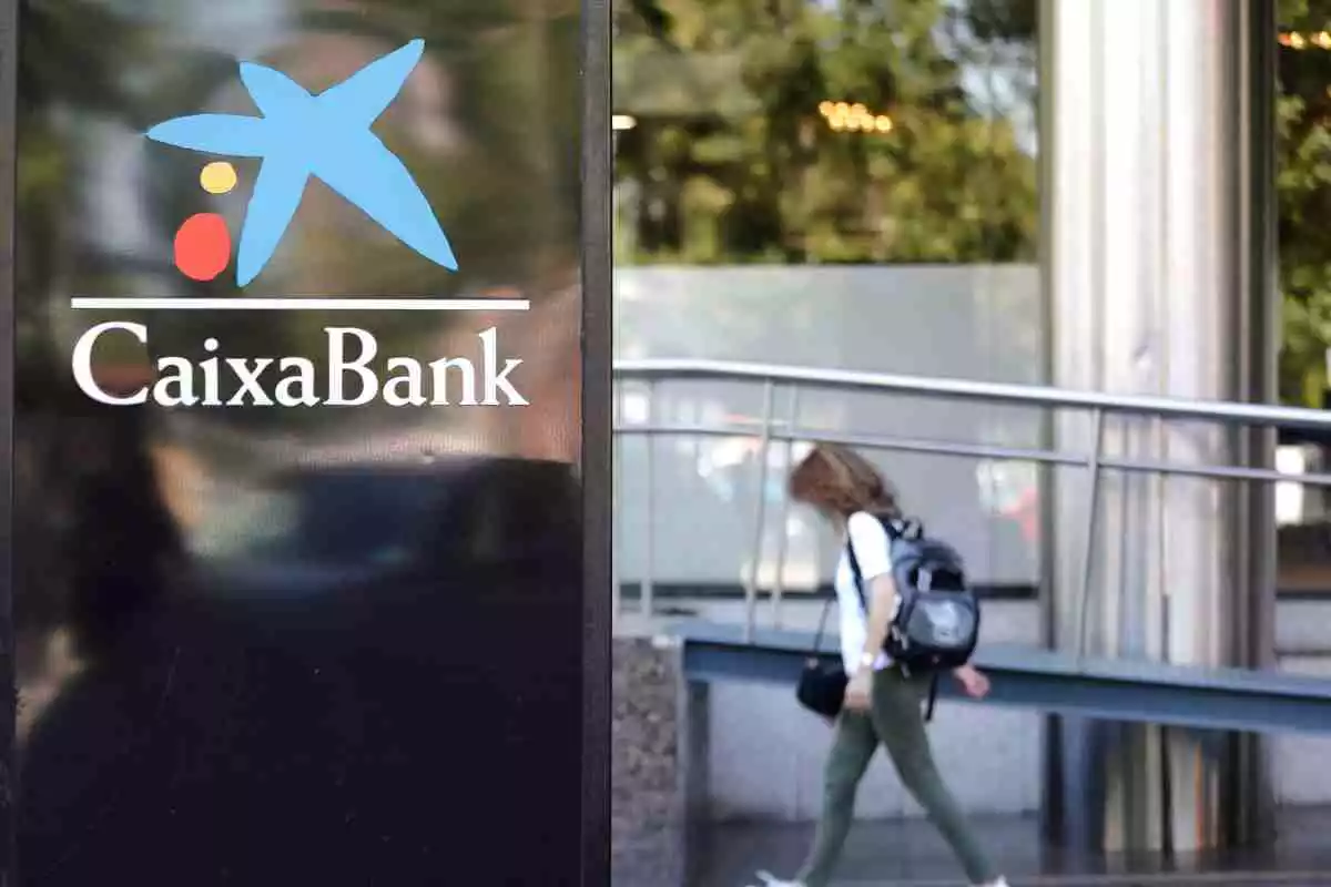El logo de CaixaBank amb una persona passant per darrere de dia