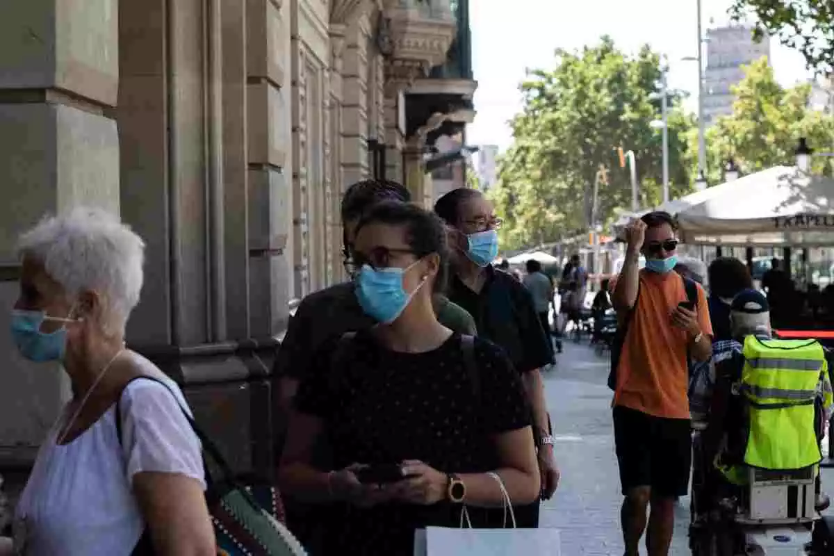 Gent amb mascareta fent cua per entrar a una biblioteca de Barcelona