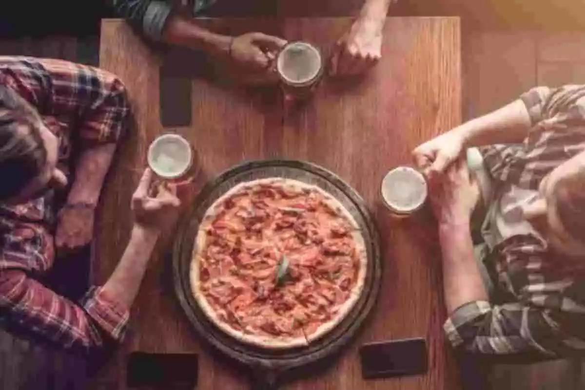 Tres nois sopant en la taula d'un restaurant amb una pizza i cerveses