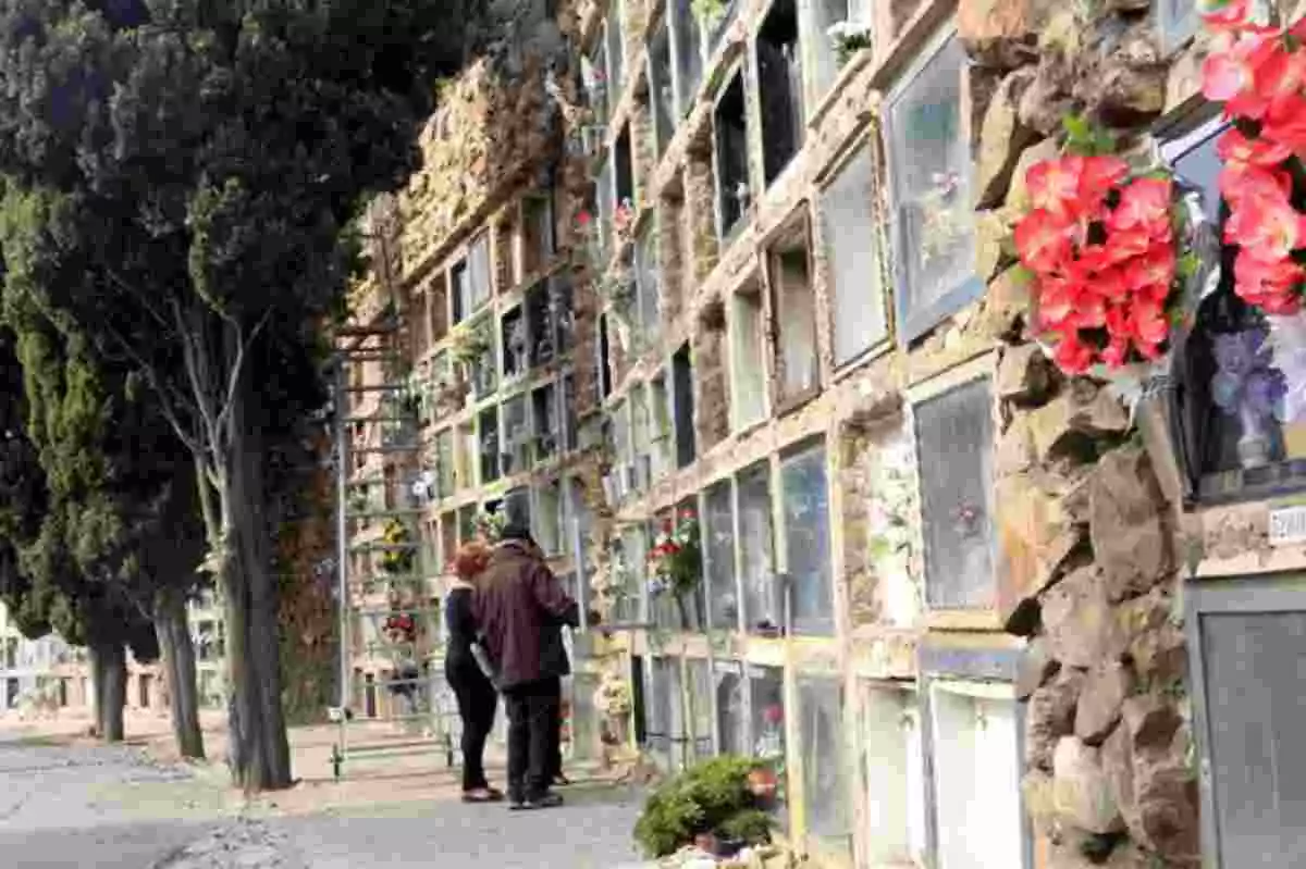 Dues persones en un cementiri de Barcelona amb molts nínxols i flors de color vermell en primer pla
