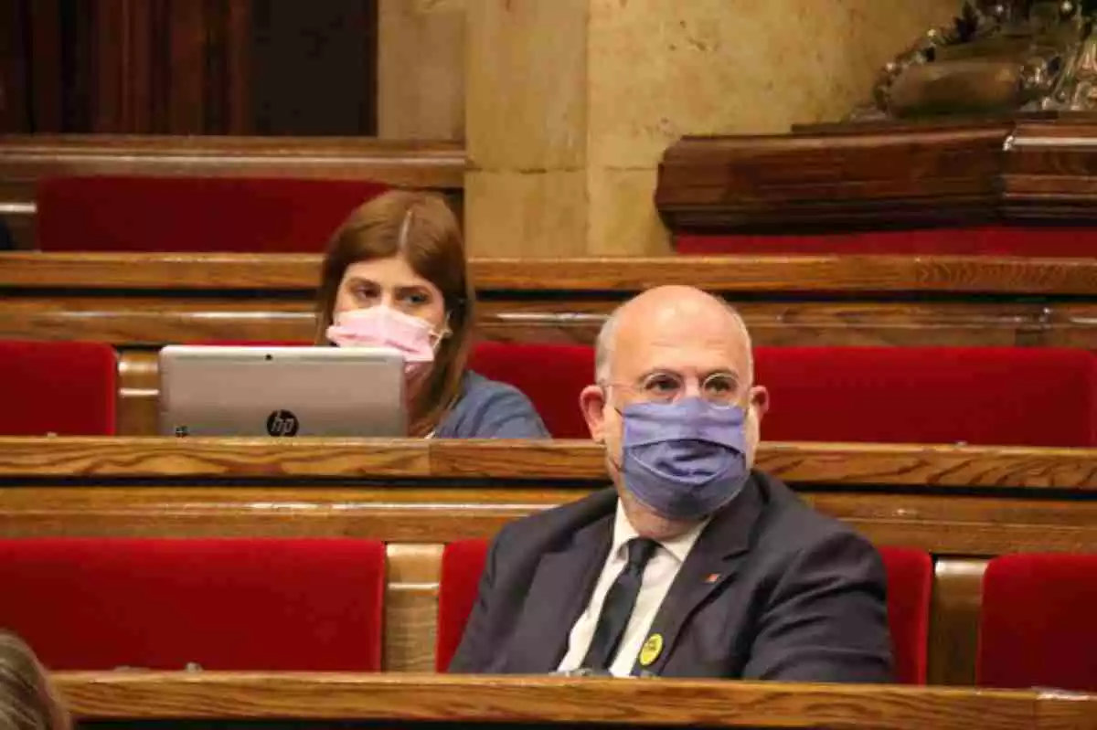 Eduard Pujol en el seu escó al Parlament de Catalunya amb mascareta posada i una dona darrere