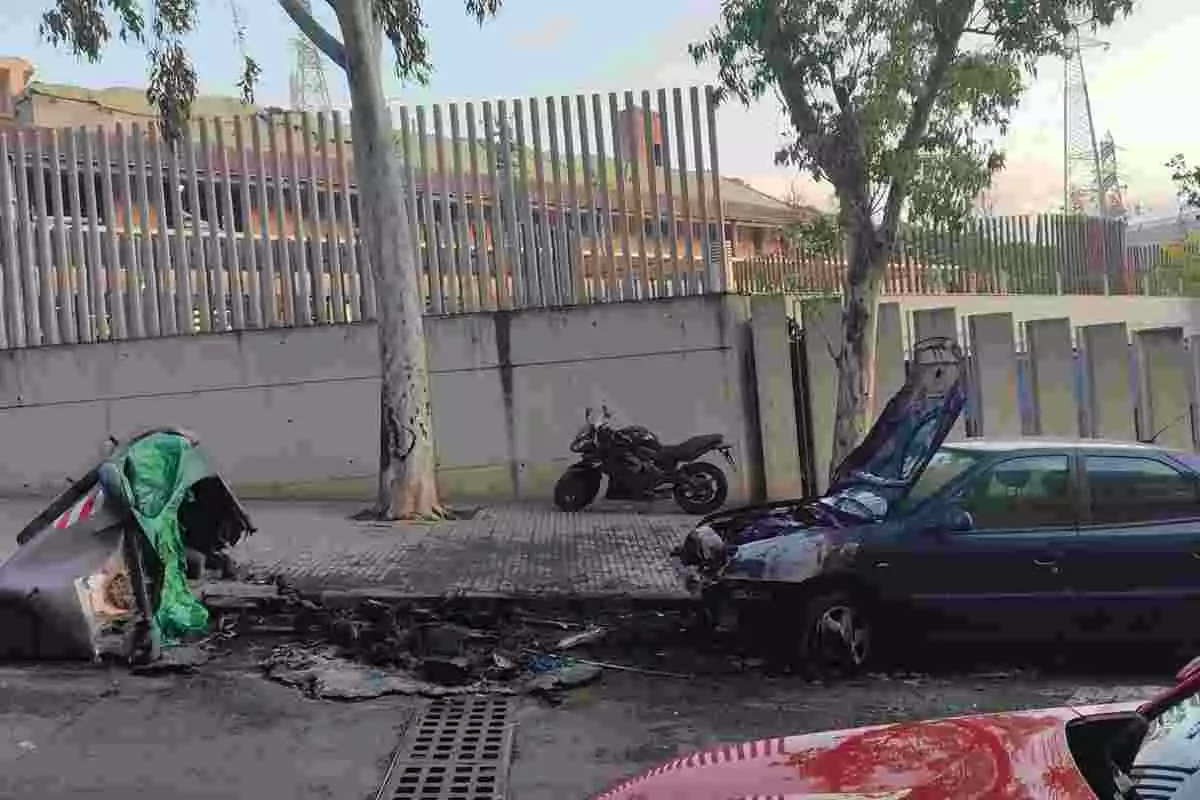 Imatge d'un contenidor calcinat i un cotxe amb la part davantera afectada, en un carrer del districte de Nou Barris