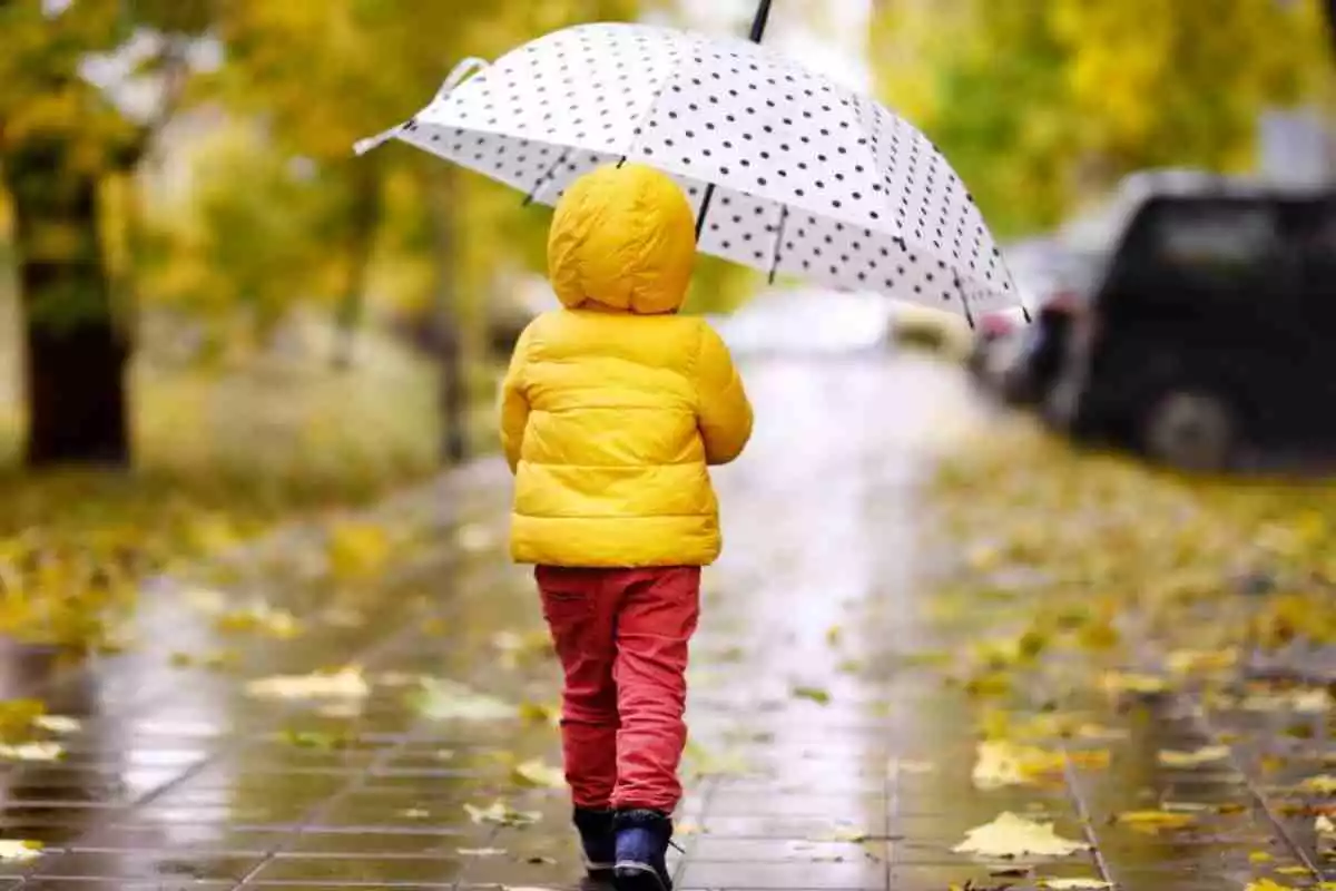 Imatge d'un menor caminant en un dia de pluja i de plena tardor