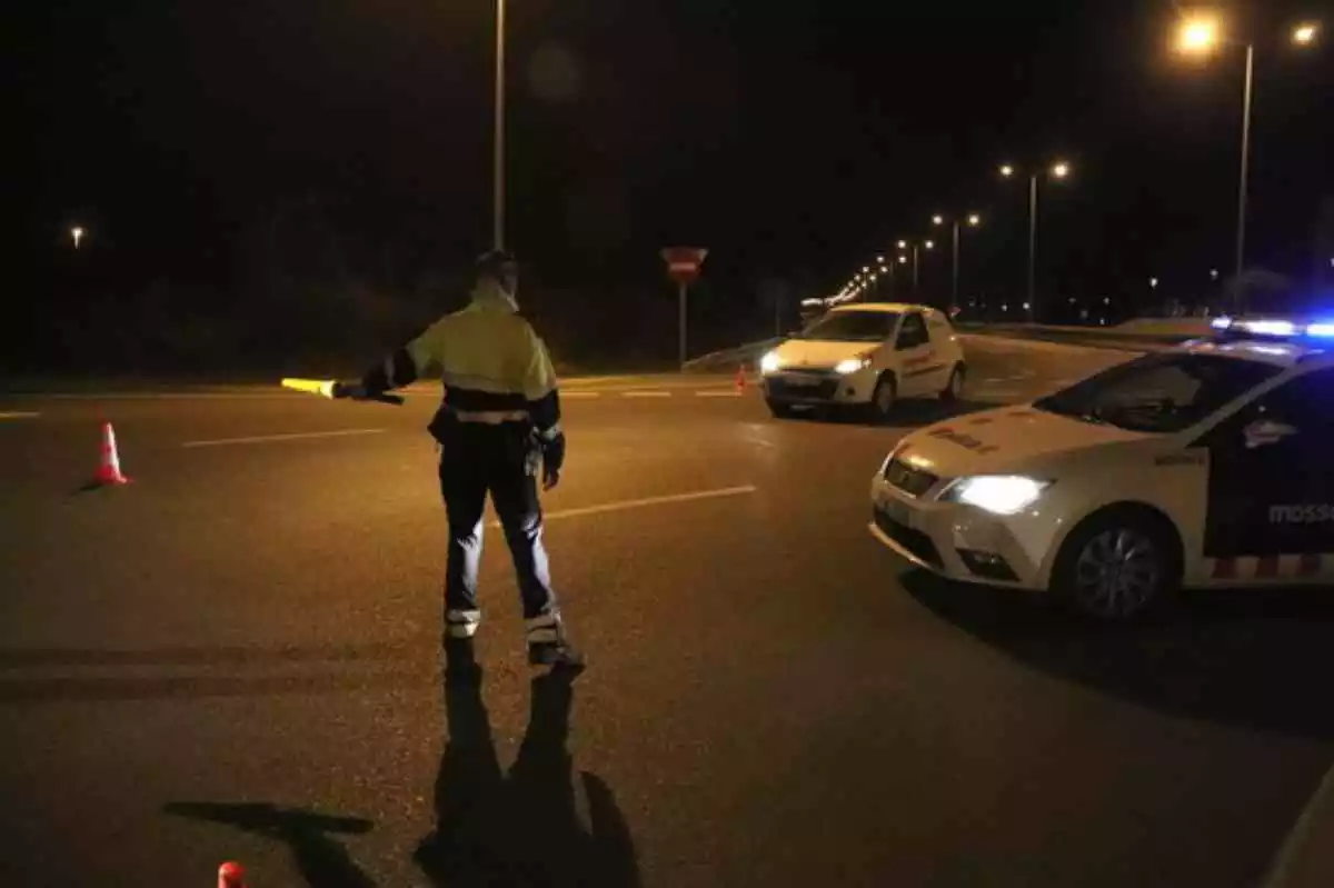 Un mosso d'esquadra de nit amb el cotxe policial al costat i un vehicle blanc apropant-se