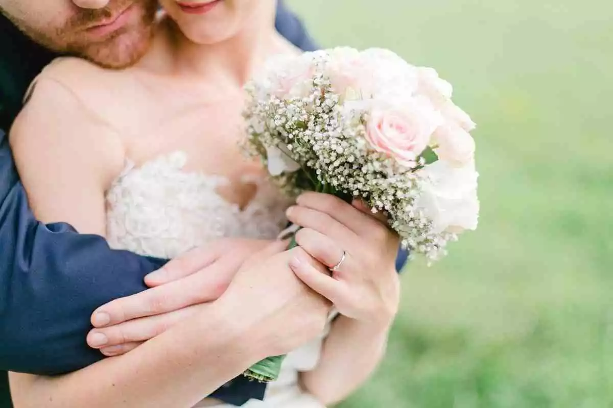 Un nuvi i una núvia abraçats agafant un ram de flors