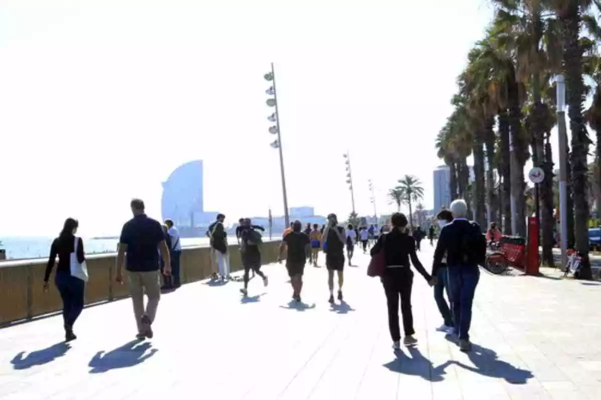 La platja de la Barceloneta de Barcelona amb persones passejant i fent esport en un dia assolellat