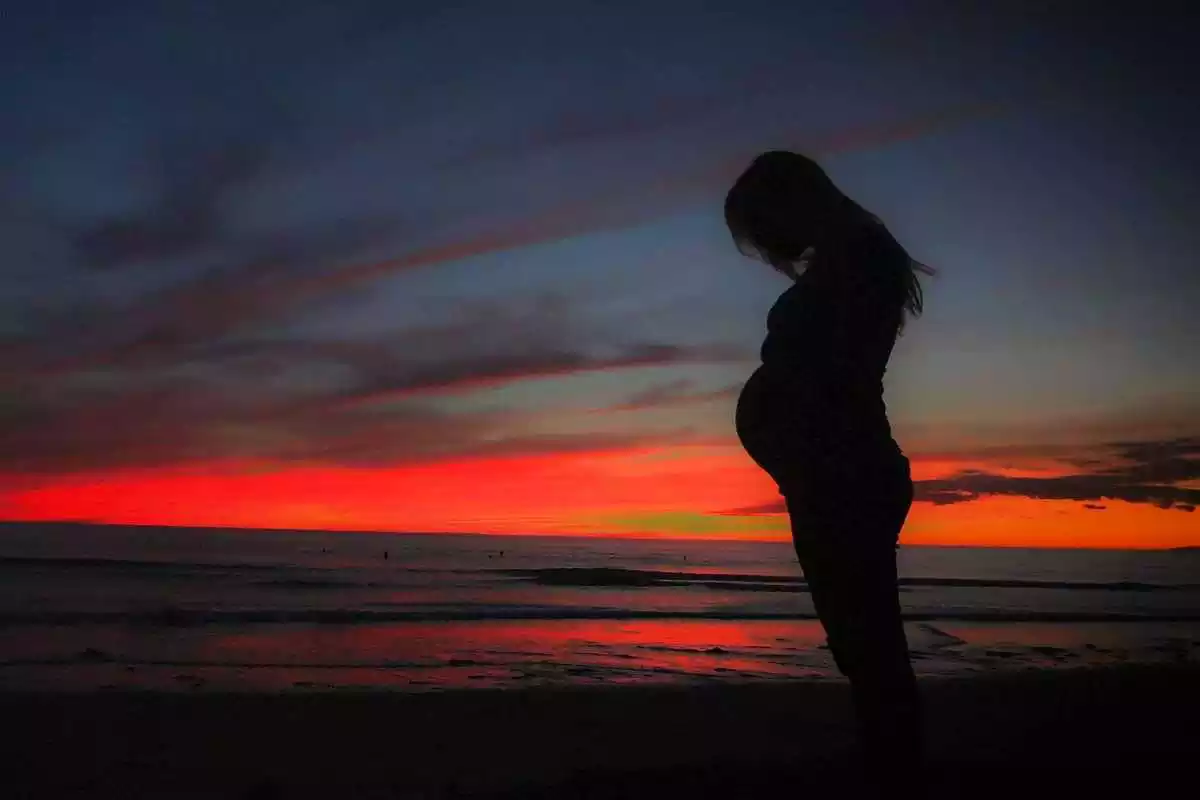 Silueta d'una dona embarassada amb una posta de sol al fons