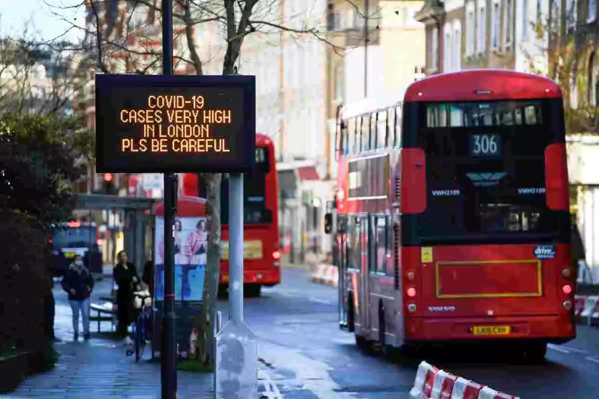 Un autobús de Londres passant pel costat d'un cartell que avisa dels casos «molt alts» de coronavirus a la zona