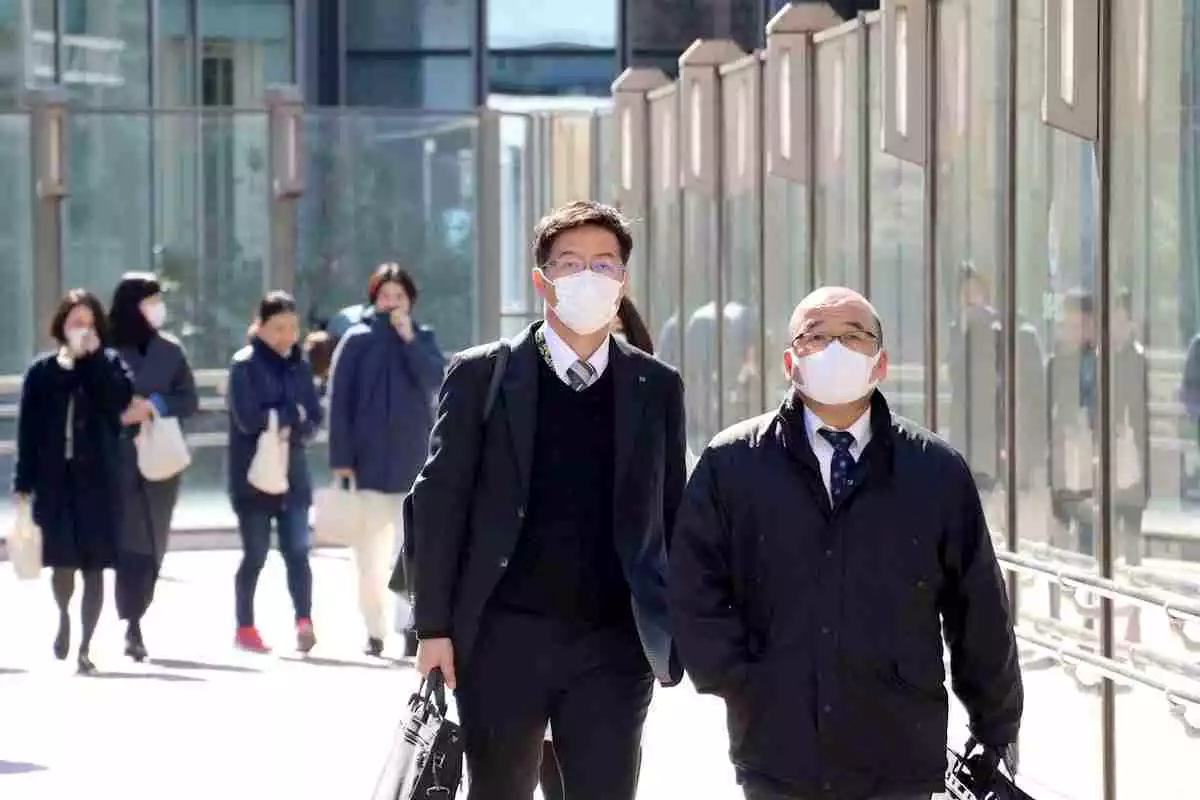 Dos homes amb mascareta en primer pla, passegen per una ciutat japonesa