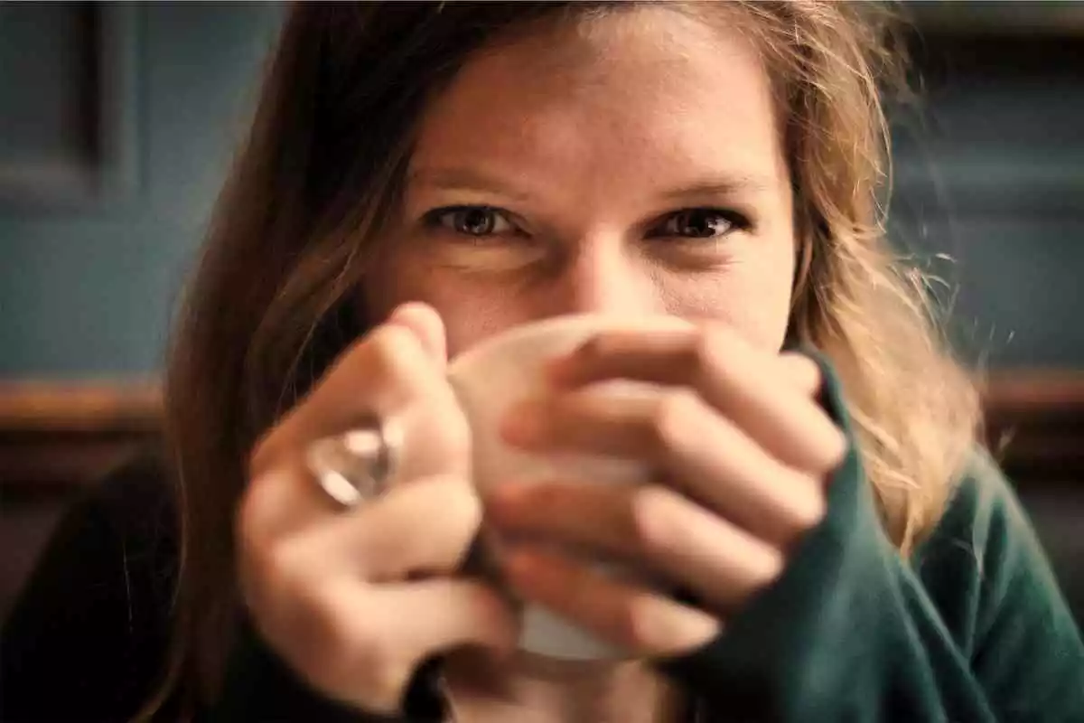 Noia amb ulls marrons bevent d'una tassa que aguanta amb les seves mans