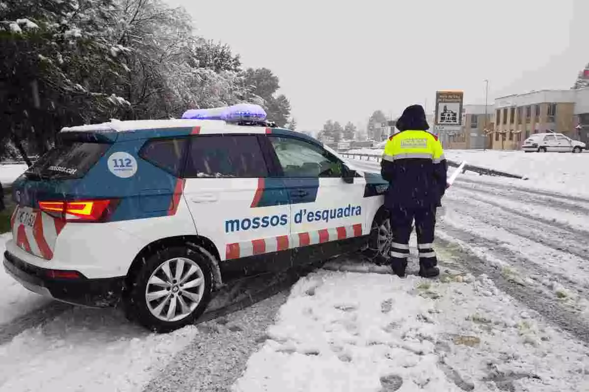 Un vehicle dels Mossos d'Esquadra amb un agent al costat en una carretera nevada