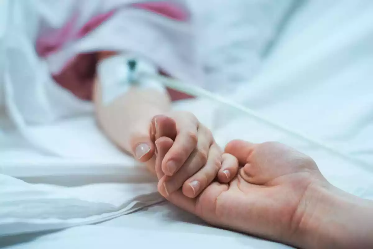 Una persona agafa una mà d'una altra al llit d'un hospital