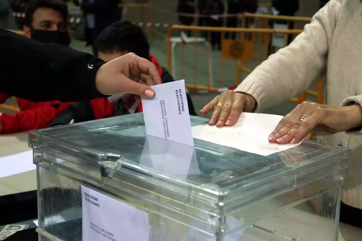 Pla detall d'una urna i de la mà d'una persona votant en un col·legi electoral