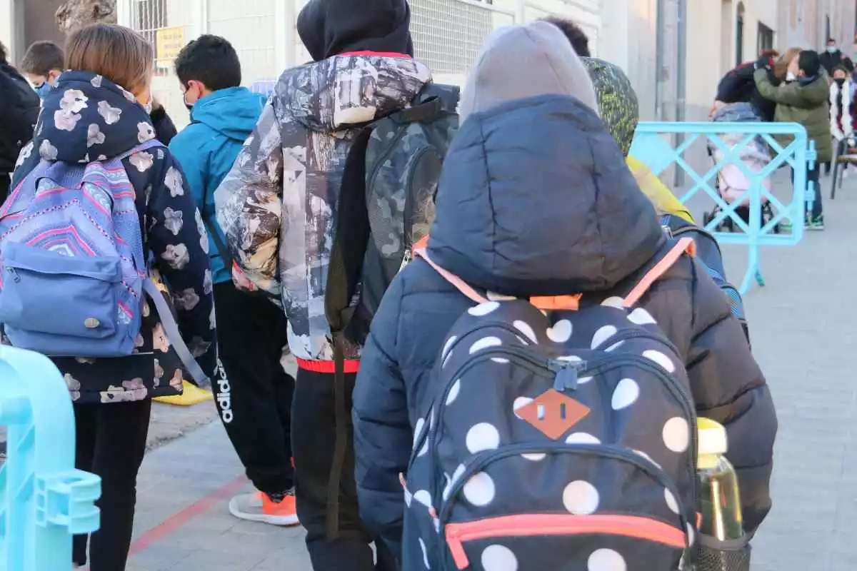 Diversos nens a l'entrada d'un centre escolar amb les seves motxilles a Figueres