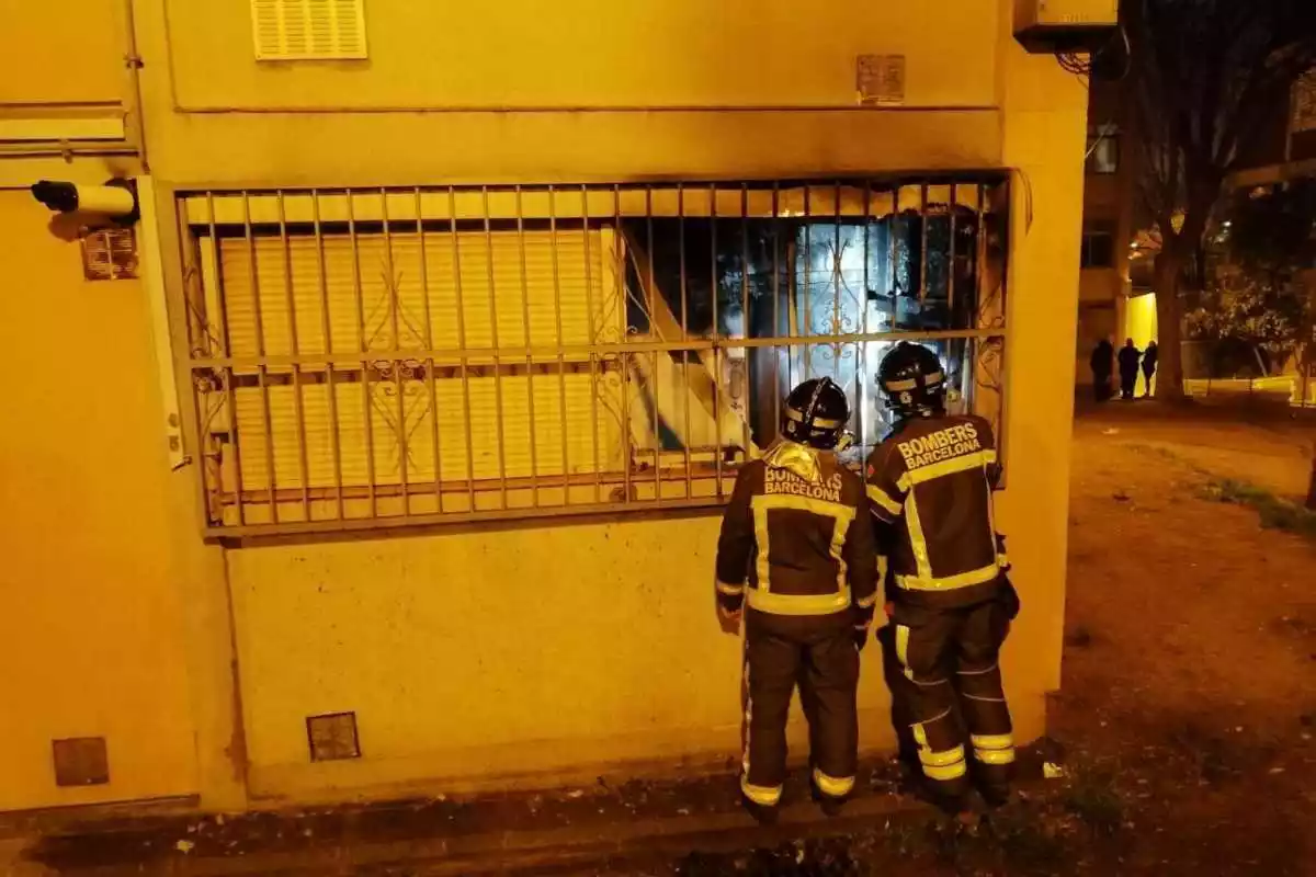 Dos bombers del cos de Barcelona a la finestra d'un habitatge incendiat de nit