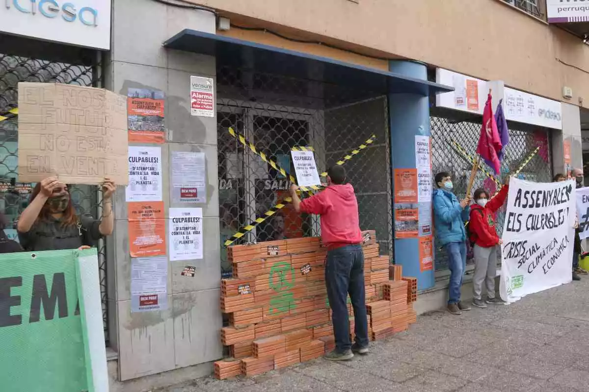 Pla mitjà lateral de l'oficina d'Endesa a Girona amb un noi col·locant un cartell a la persiana