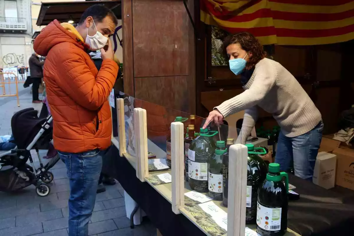 Pla obert d'un comprador i d'una venedora en un dels estands de la 20a edició de la fira de l'oli nou DOP Siurana de Tarragona
