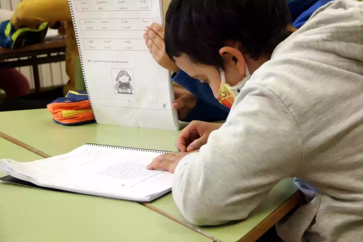 Un nen escriu en un llibre en un centre escolar de Catalunya amb la mascareta posada