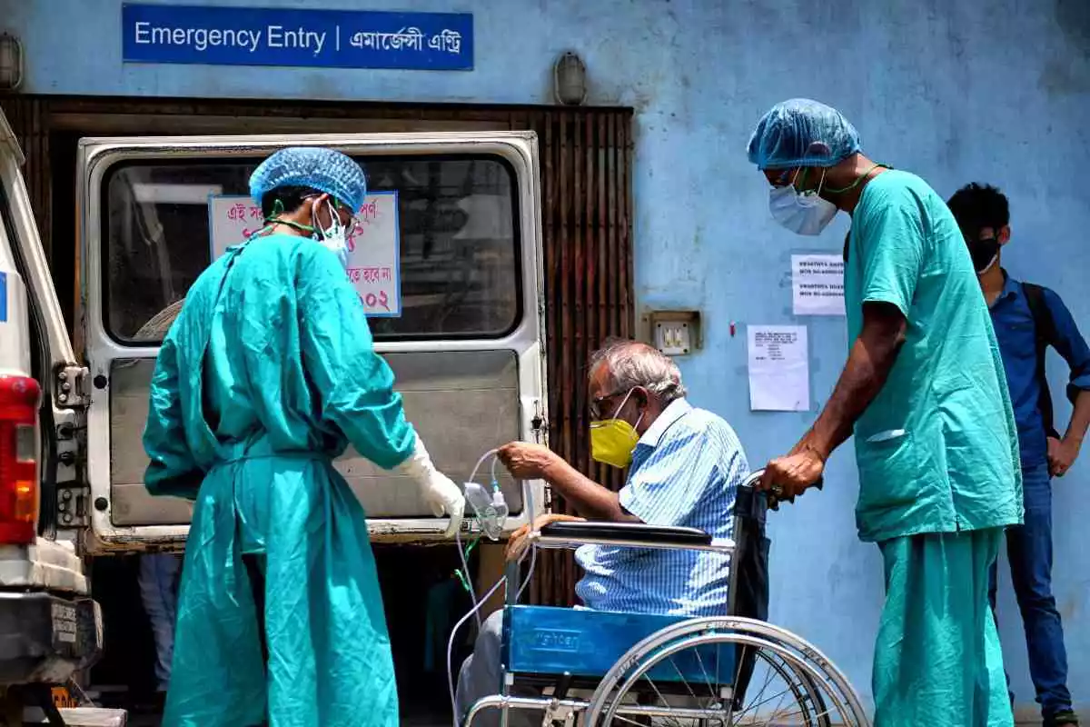 Imatge d'un malalt en cadira de rodes a l'Índia, acompanyat de dos sanitaris