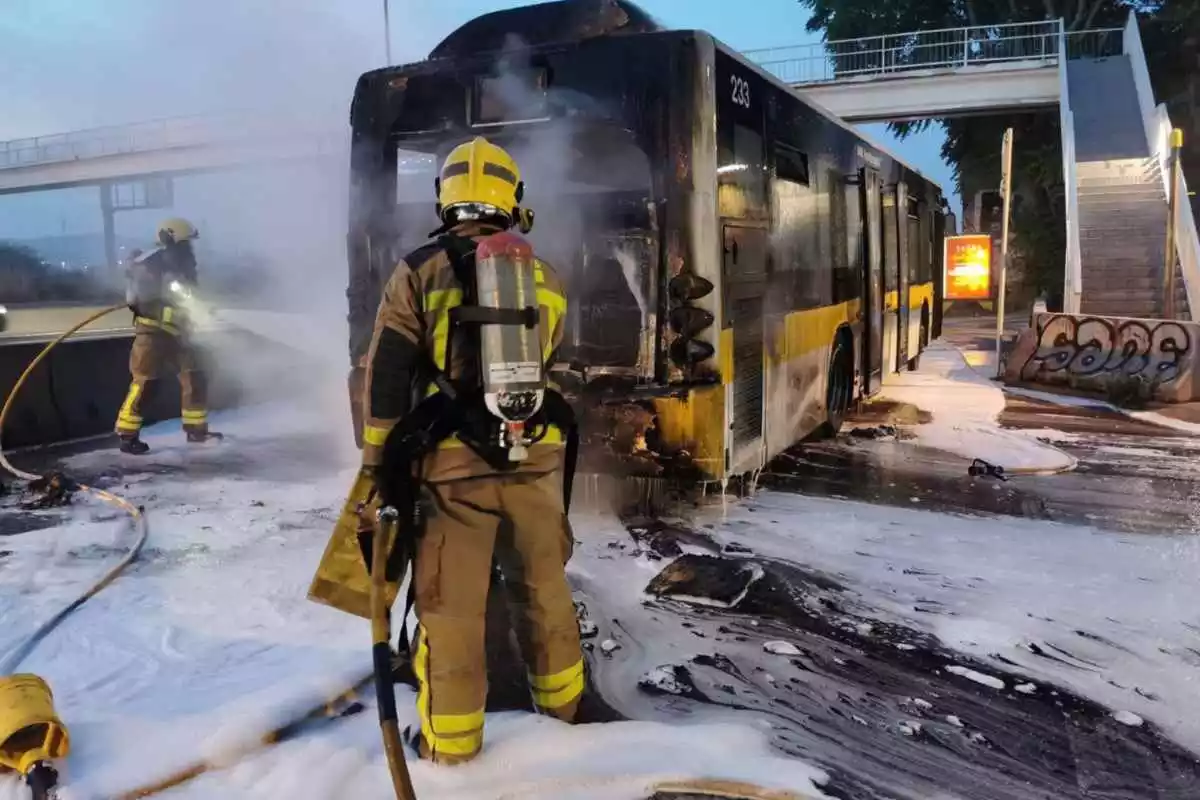 Imatge de dos bombers apagant les flames que han calcinat l'autobús