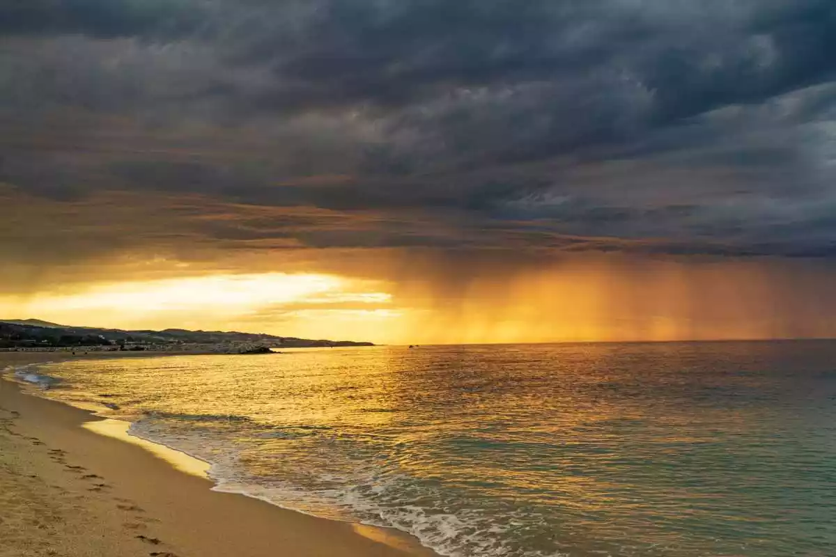 Imatge d'una sortida de sol amb la presència de núvols i traces de precipitació des de la platja de Mataró