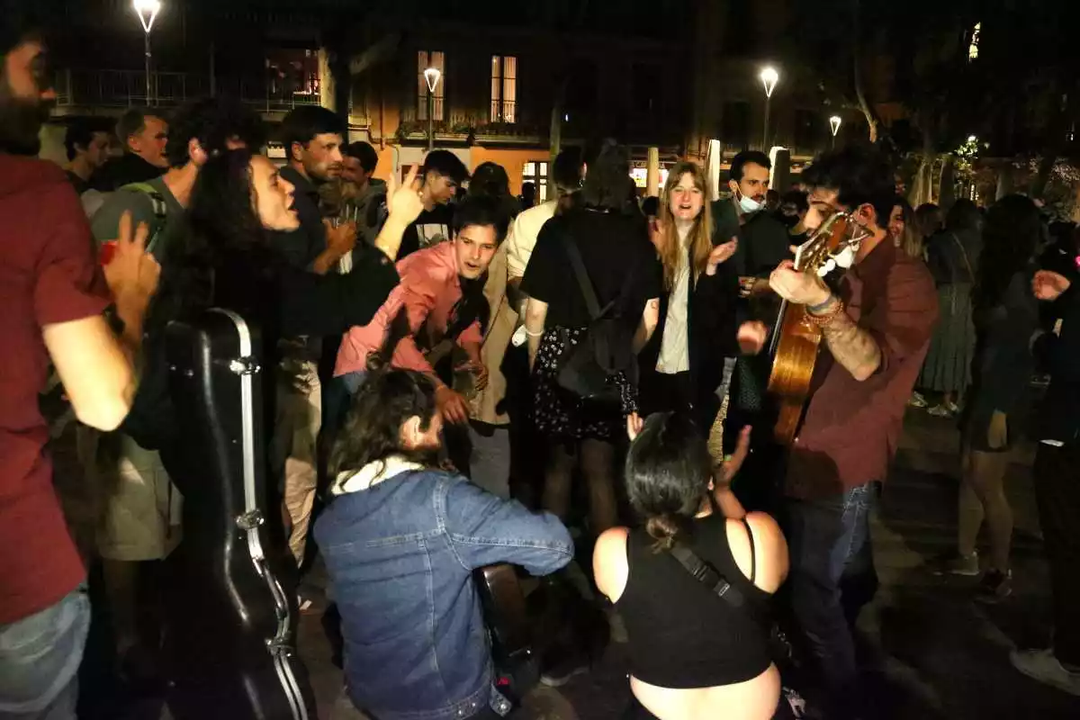 Pla obert de diversos joves sense mascareta i cantant amb guitarres celebrant el final del toc de queda a la plaça de la Virreina de Gràcia