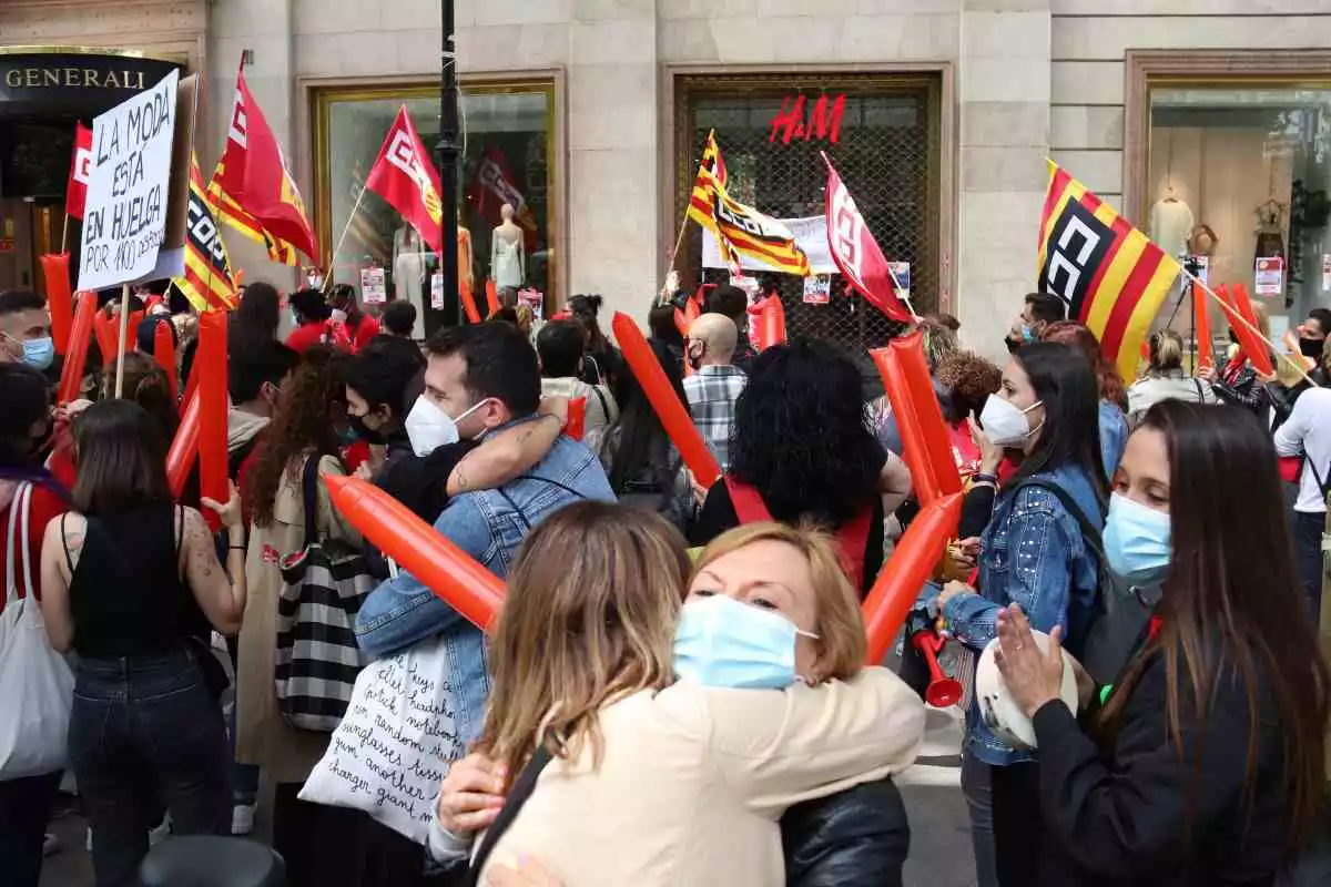 Pla obert de manifestants abraçant-se a la concentració de treballadors d'H&M davant d'una de les botigues de la marca al Passeig de Gràcia