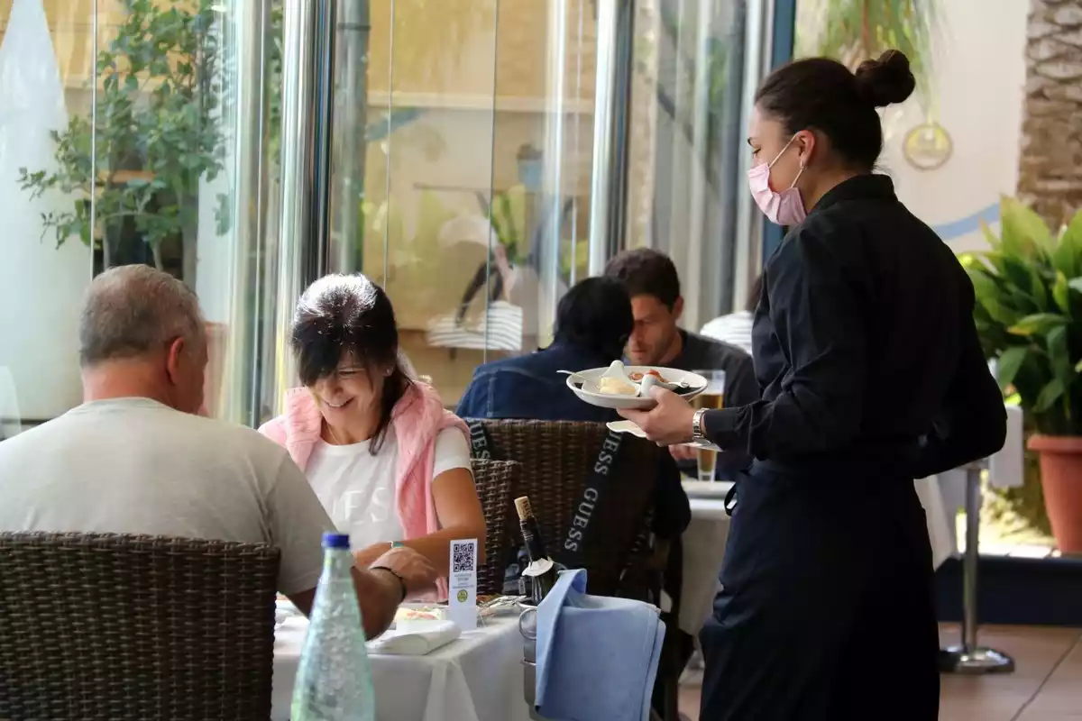 Imatge d'una cambrera en un restaurant de Sant Carles de la Ràpita servint a dos clients en un restaurant