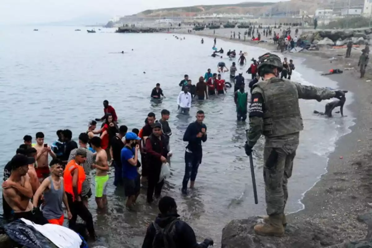 Un militar de l'exèrcit espanyol dona instruccions a diversos immigrants que acaben d'arribar a la costa de Ceuta i que encara es troben al mar