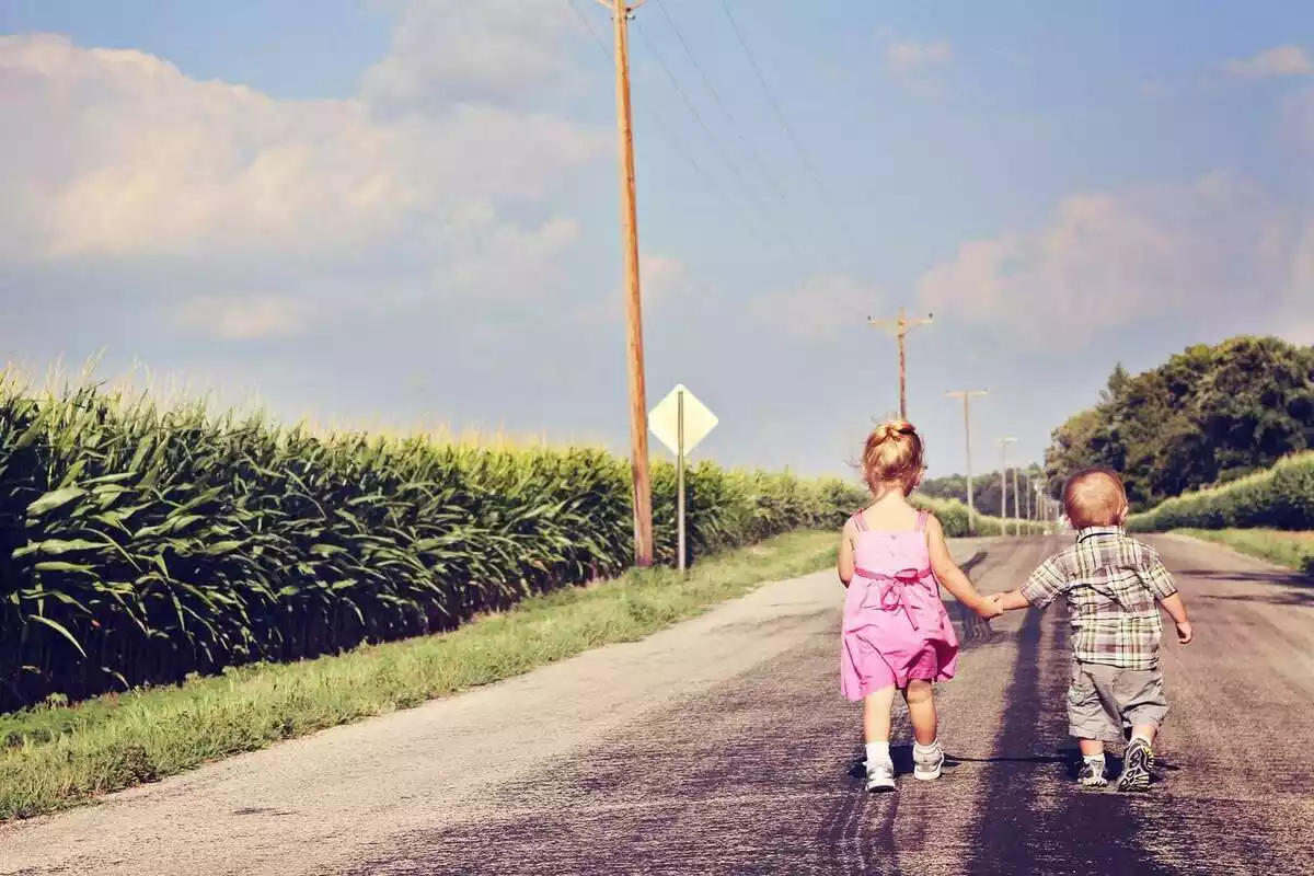 Dos nens agafats de la mà i caminant sols per una carretera