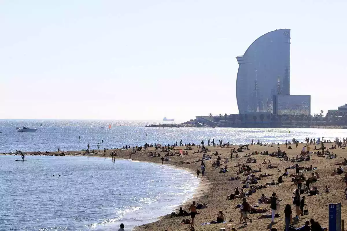 Imatge de la platja de la Barceloneta a Barcelona, plena de gent, amb vistes a l'Hotel Vela