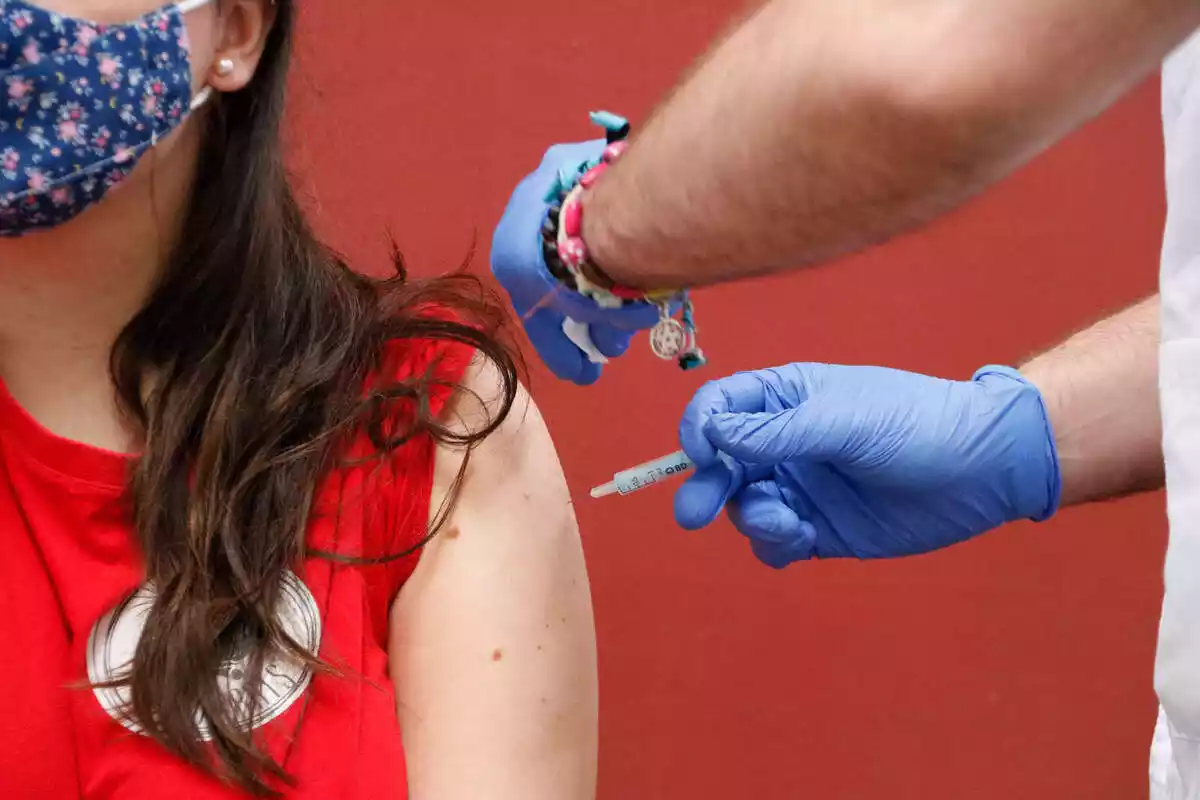 Imatge d'un infermer posant la vacuna a una noia amb samarreta vermella