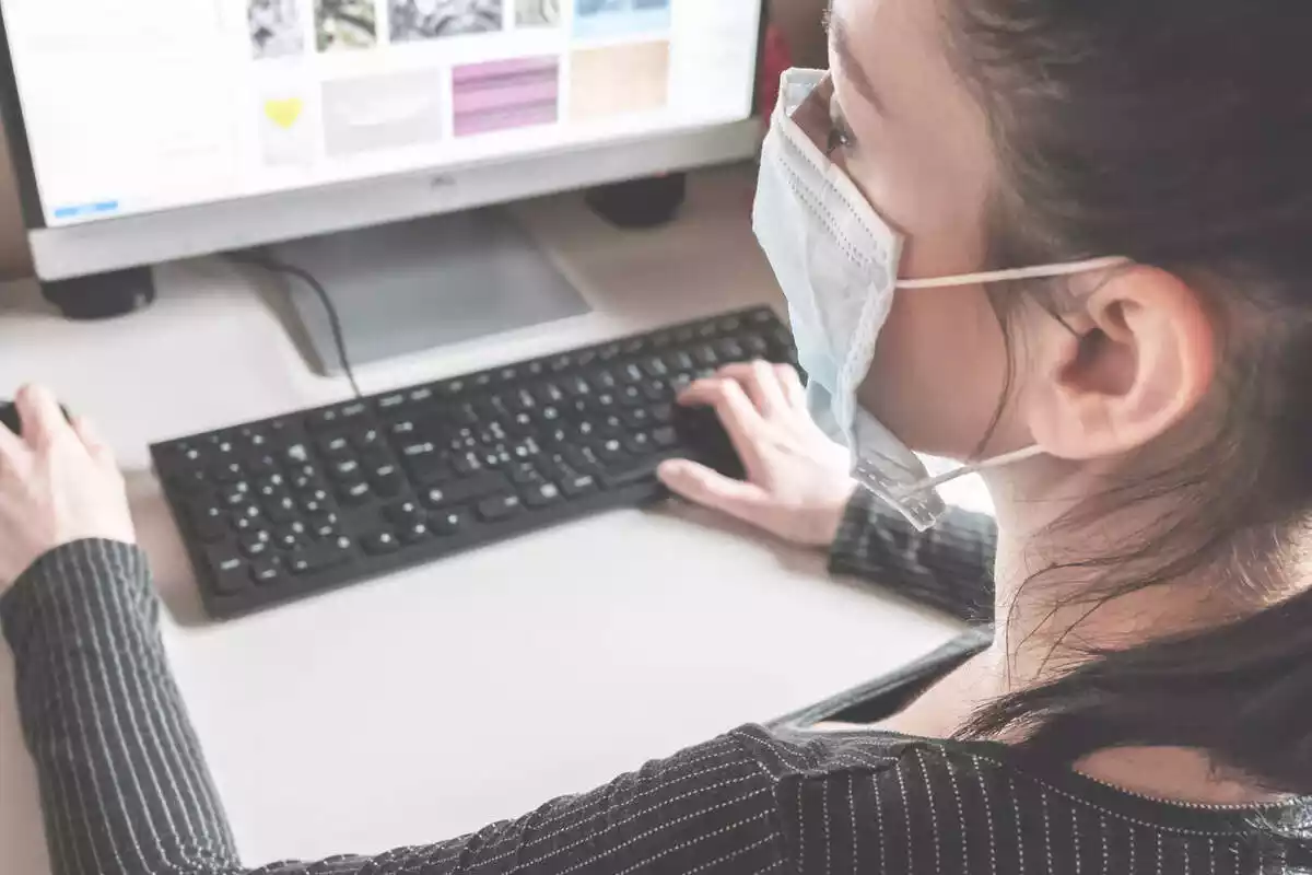 Una dona jove que treballa a l'ordinador amb mascareta